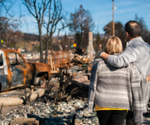 A man has his arm around a woman to comfort as they view their burned home.