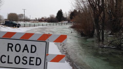 Road closed sign in front of a flooded road in the winter.
