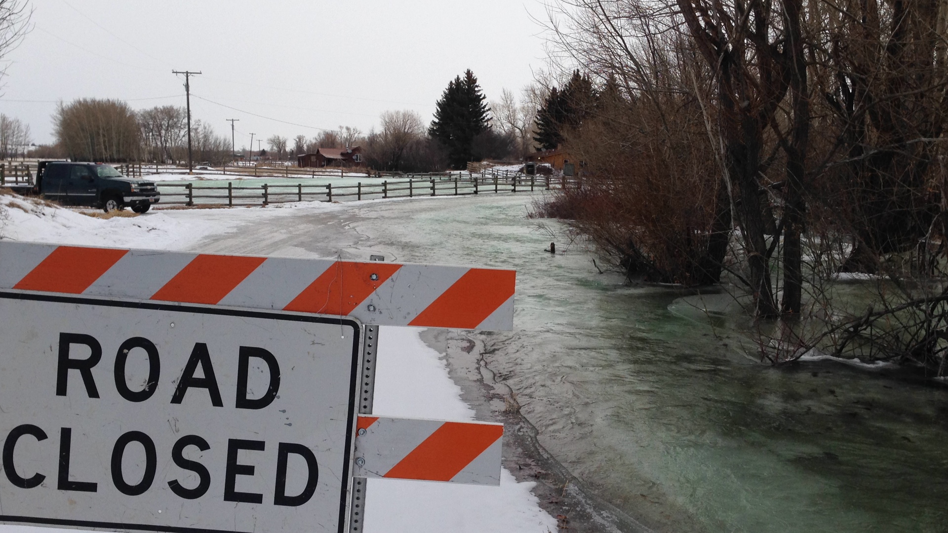Road closed sign in front of a flooded road in the winter.